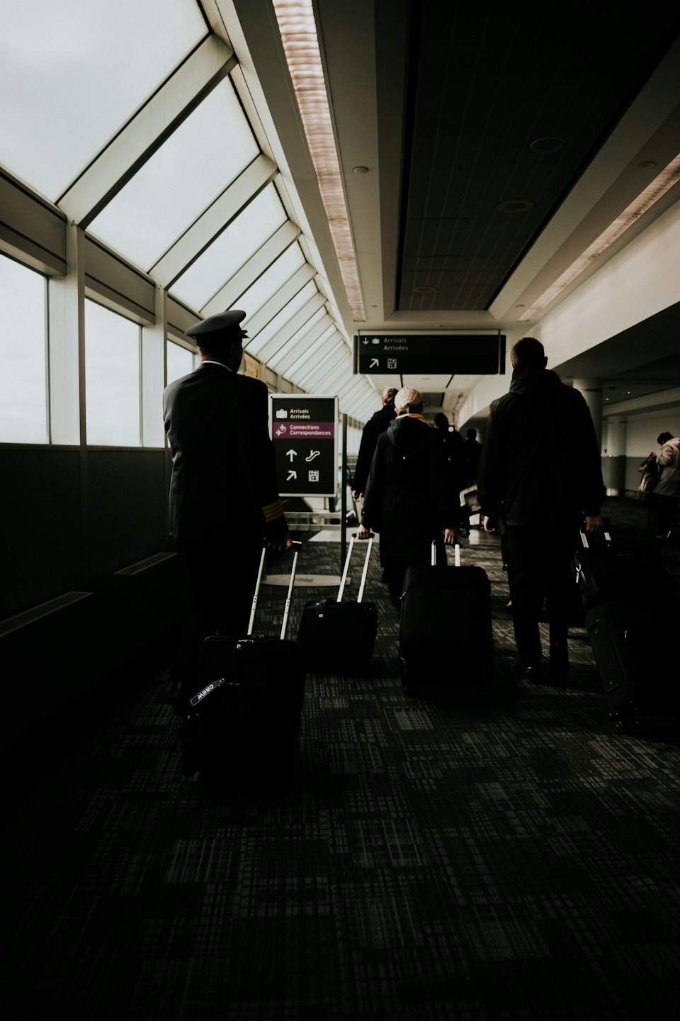 Un pilota e viaggiatori trascinano i bagagli attraverso un terminal aeroportuale.