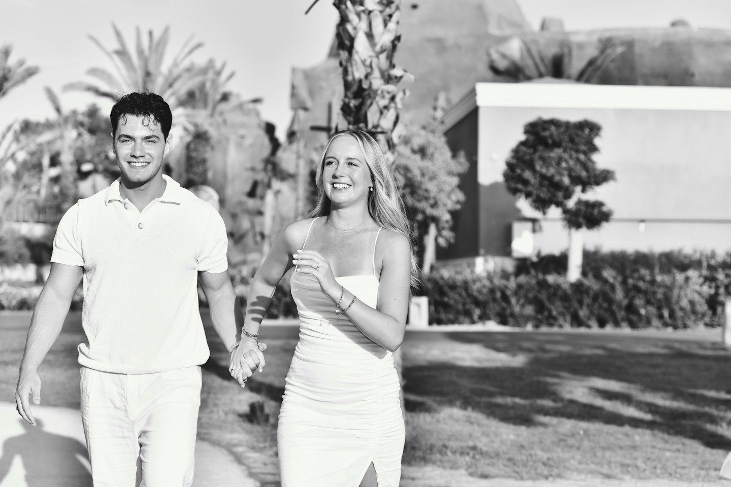 Una coppia sorridente cammina mano nella mano su un sentiero lastricato di un resort.