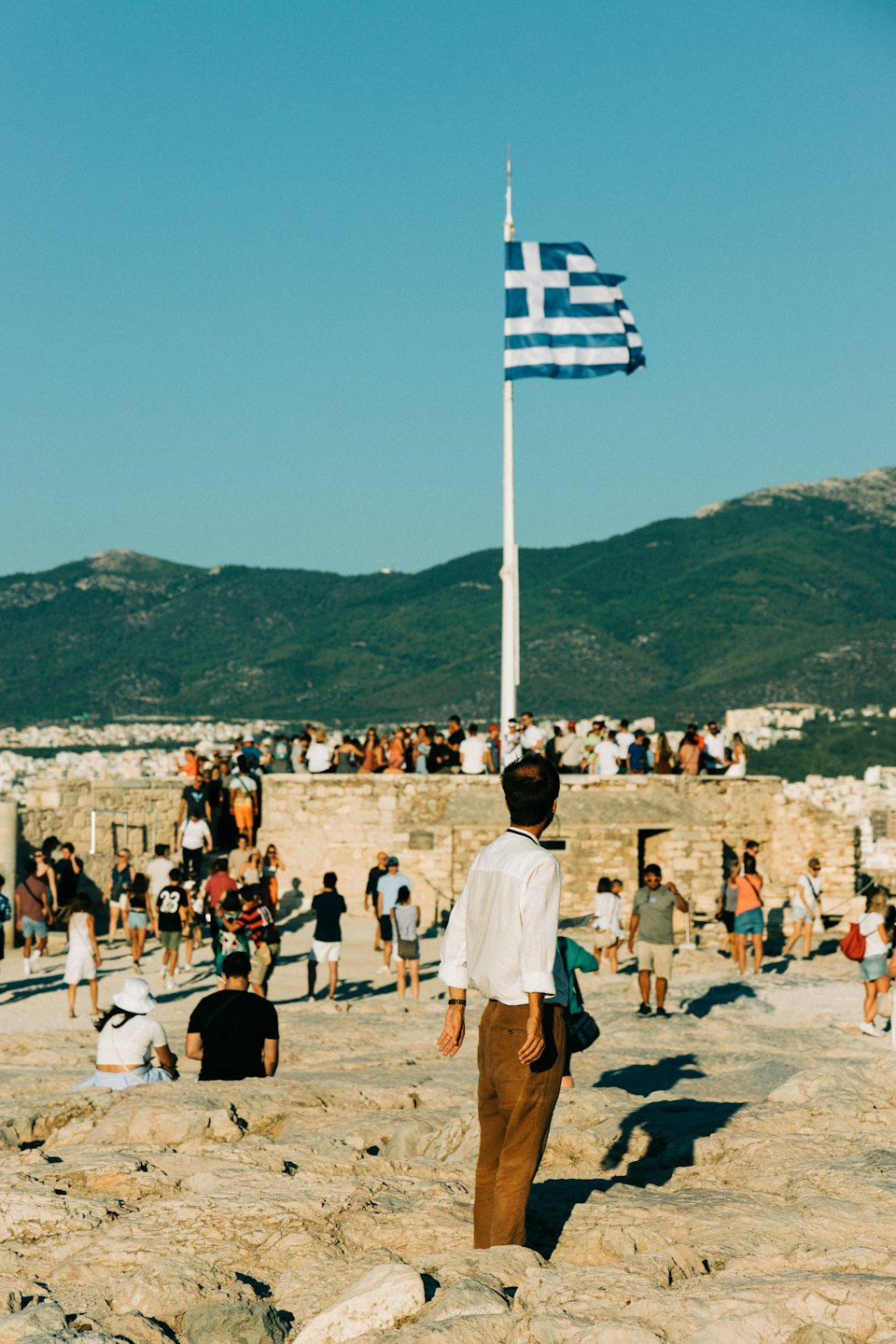 Turisti esplorano antiche rovine di pietra vicino a una bandiera greca.